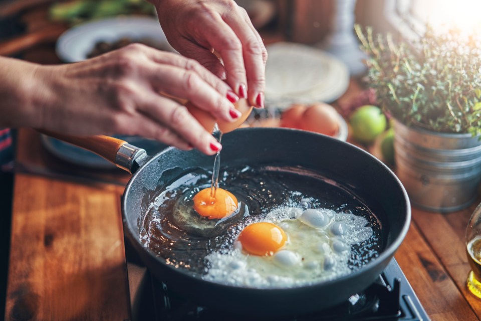 Two eggs being cracked and fried in a pan.