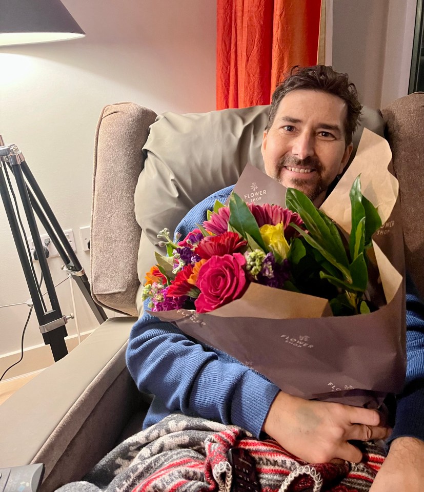 Man sitting in a recliner holding a bouquet of flowers.