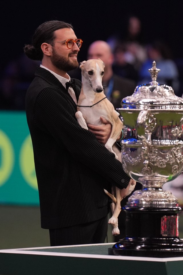 Man holding a whippet dog and a trophy.