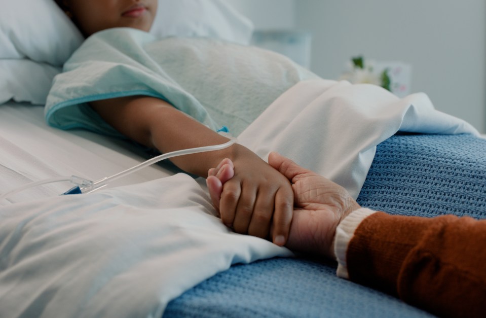 A child in a hospital bed holding hands with an adult.