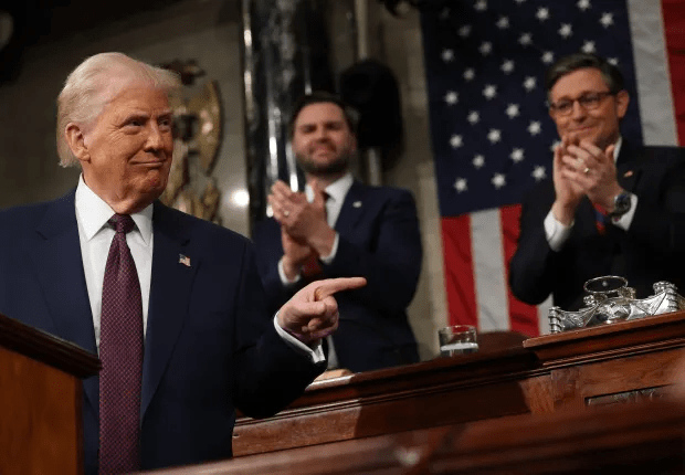 Donald Trump speaking at a podium, with two men applauding behind him.