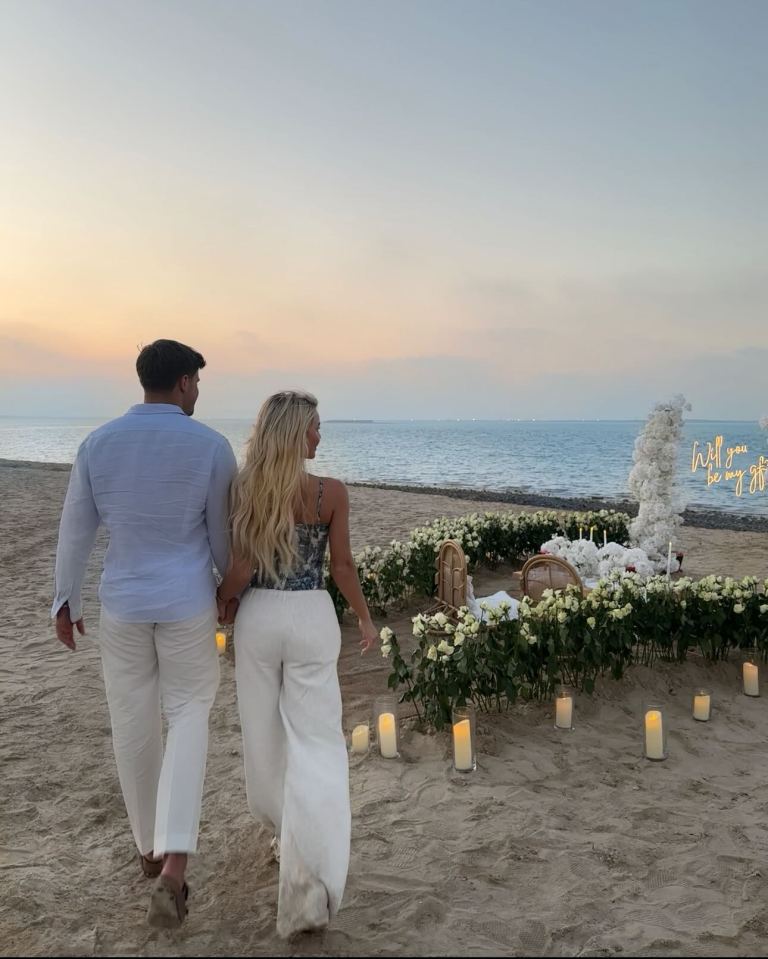 Couple walking toward a romantic beach proposal.