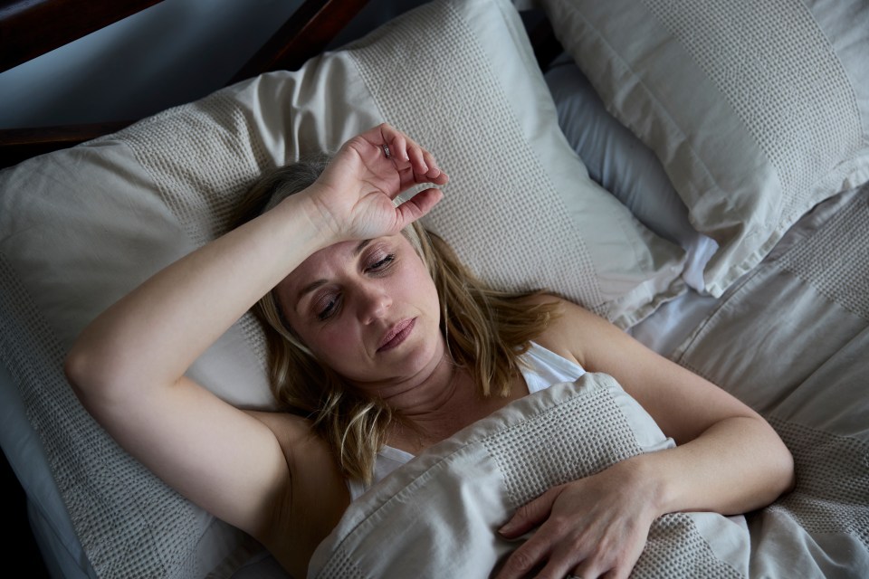 Woman lying in bed, hand on forehead, appearing to suffer from insomnia.