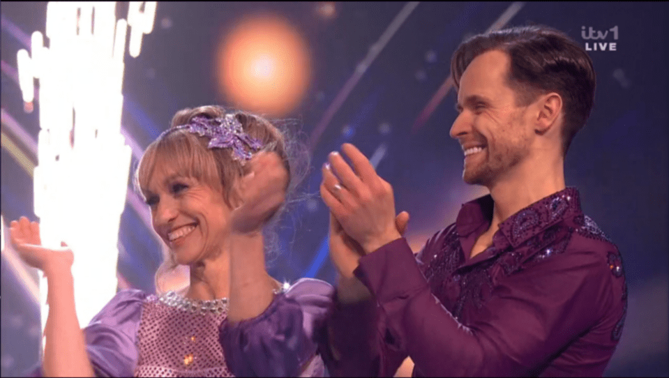 Two smiling people in purple outfits clapping.