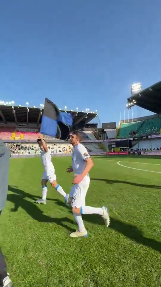 Two soccer players running on a field, carrying a flag.