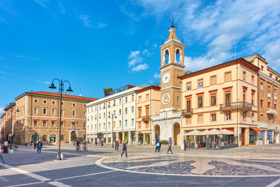 Piazza Tre Martiri in Rimini, Italy, with a clock tower and surrounding buildings.