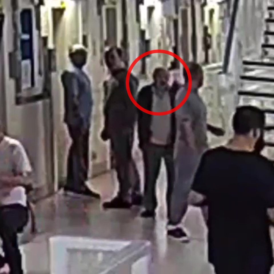 Security camera image of a man surrounded by a group of people in a hallway.