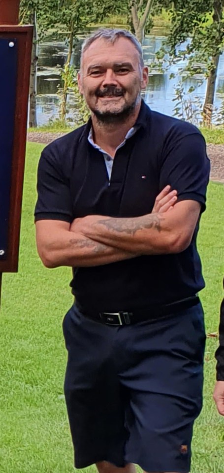 Man with arms crossed standing on a golf course.