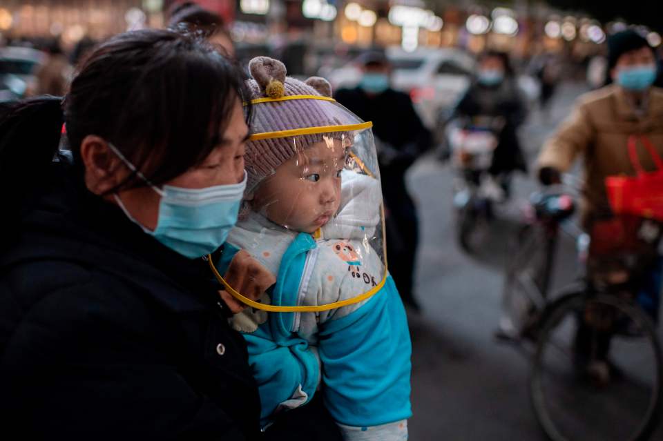 Woman wearing a face mask holds a baby wearing a face shield.